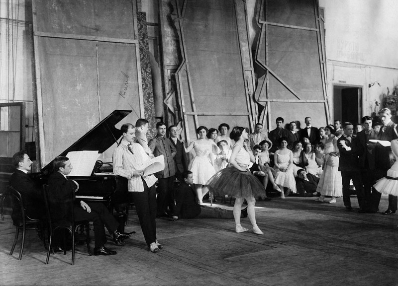 Ballets Russes während der Probe: Am Klavier rechts sitzt der Komponist Igor Strawinsky. Daneben stehend: Michael Fokine. In der Mitte steht die Ballerina Tamara Karsawina.