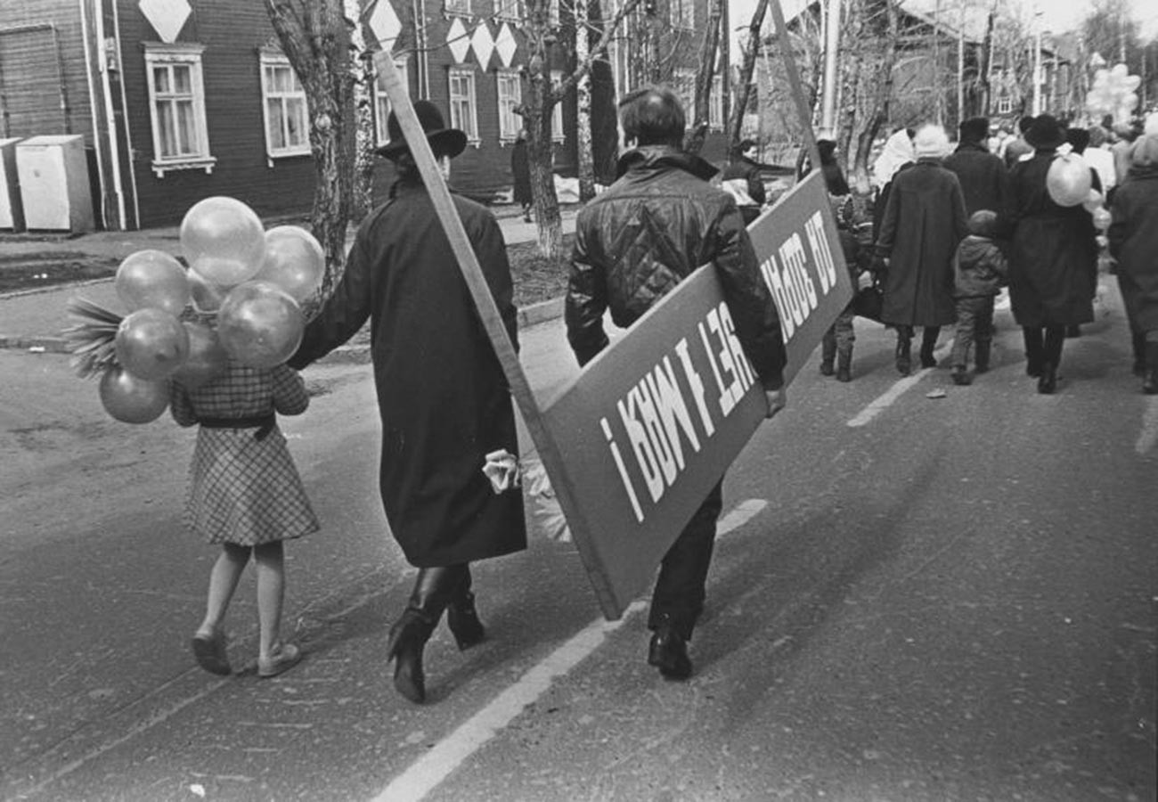 Un homme avec une pancarte «Vive le 1er mai» se rend à une manifestation avec sa famille, 1987
