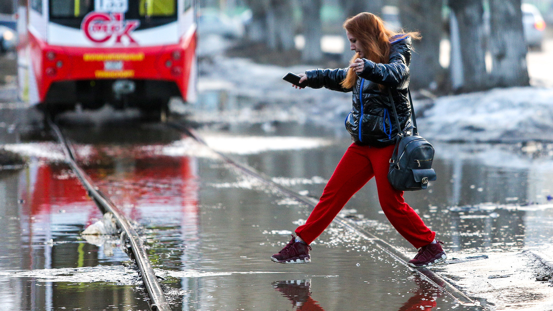 Омск, 7 апреля 2021 года: Женщина переступает через воду на затопленной улице. Наводнение вызвано таянием снега
