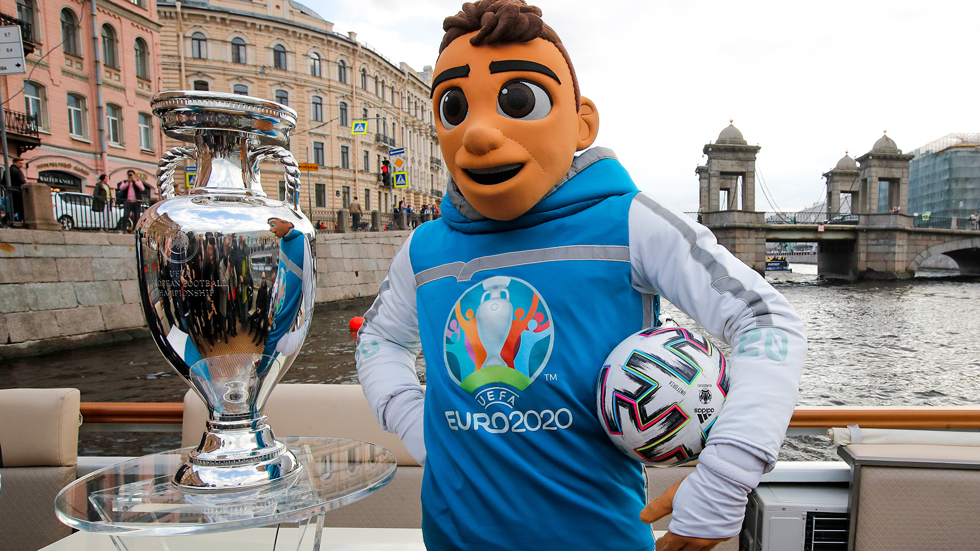 EURO 2020 championship mascot Skillzy poses with the EURO 2020 trophy traveling on a boat down the Fontanka River during the official EURO 2020 trophy's tour in St.Petersburg, Russia, Saturday, May 22, 2021. St. Petersburg will host seven postponed UEFA EURO 2020 matches, including a quarter final.
