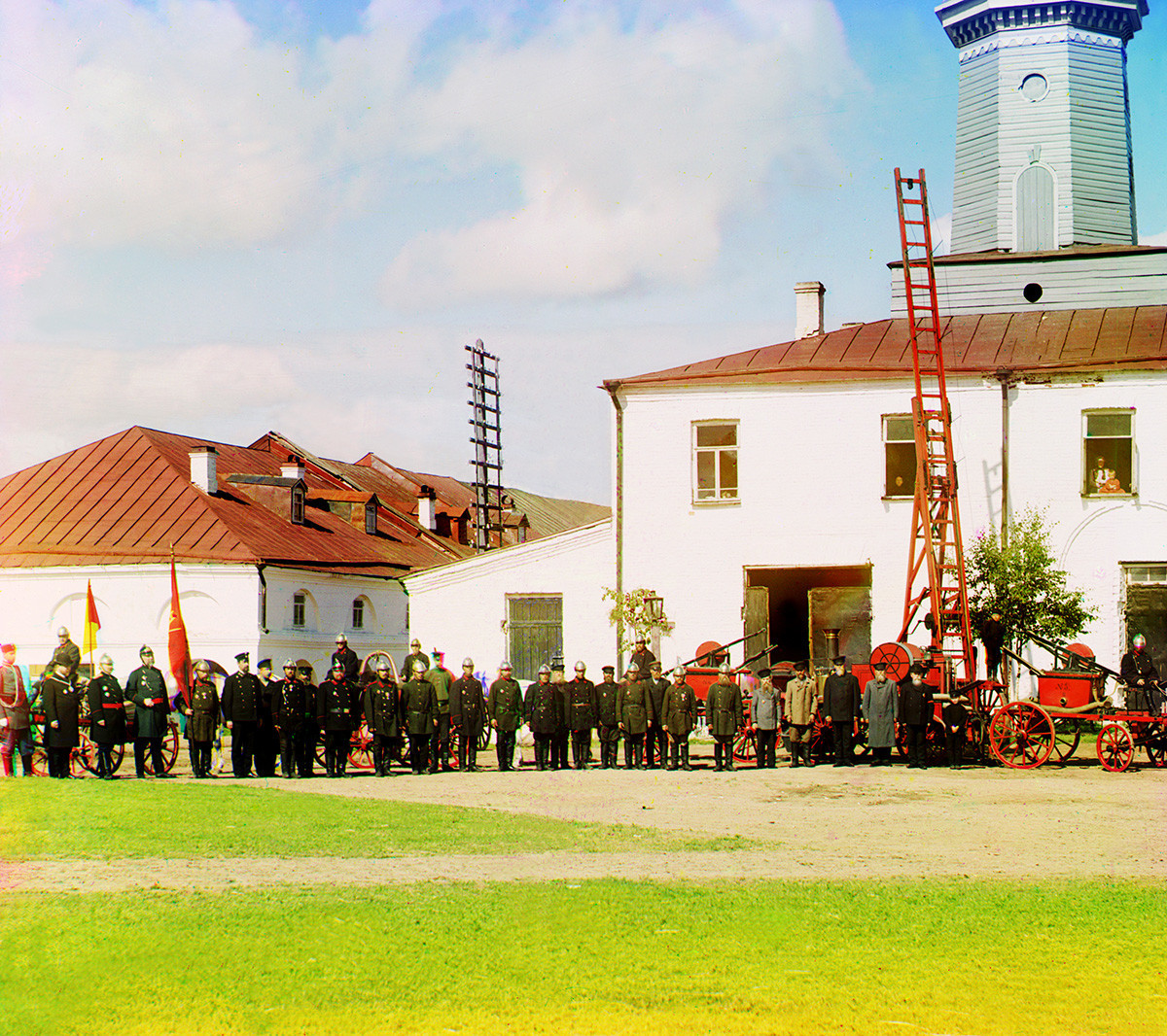 Gasilska postaja in stražni stolp s člani gasilske enote in lokalne uprave. Levo: delni pogled na trgovske arkade. Poletje 1909
