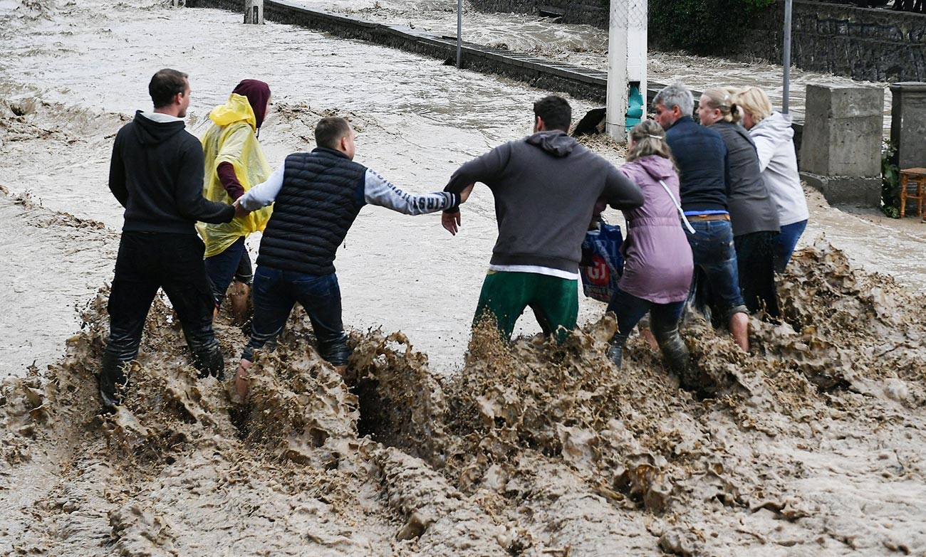 Ljudi pomažu jedni drugima da prijeđu ulicu u Jalti. Krim su zadesile obilne padavine koje su prouzrokovale poplave.
