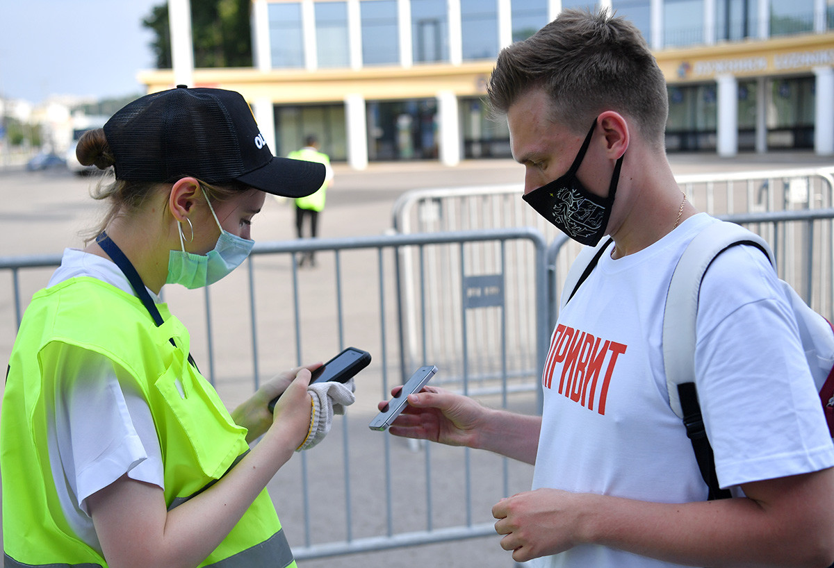 モスクワのルジニキ・スタジアムでUEFAユーロ2020のファンゾーン入り口の前にCOVID-19ステータスを証明するQRコードを提示する男性。Tシャツに「ワクチン接種を受けた」とプリントされている。