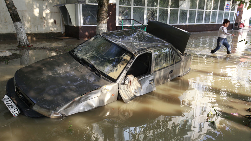Seorang penduduk setempat melewati sebuah mobil rusak yang terjebak di jalan yang terendam banjir di Kota Krymsk, Krasnodarsky krai, Rusia.