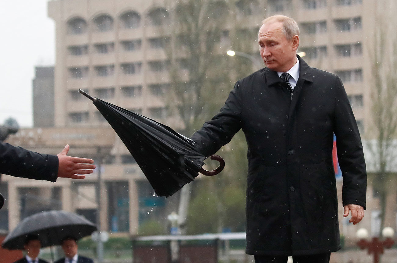 Putin predaja dežnik asistentu pred polaganjem cvetja pred obeležjem Večni ogenj v Biškeku v Kirgiziji, 28. marca 2019.