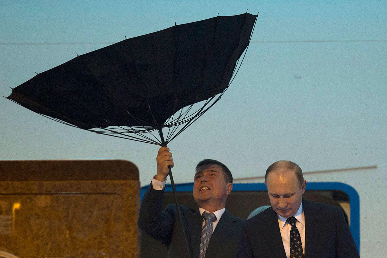 Служител по сигурността се бори с чадър, докато президентът на Русия Путин излиза от самолет при пристигане на летището преди четвъртата среща на върха на Конференцията за мерки за изграждане на взаимодействие и доверие в Азия (CICA), проведена в Шанхай. 19.05.2014 г.
