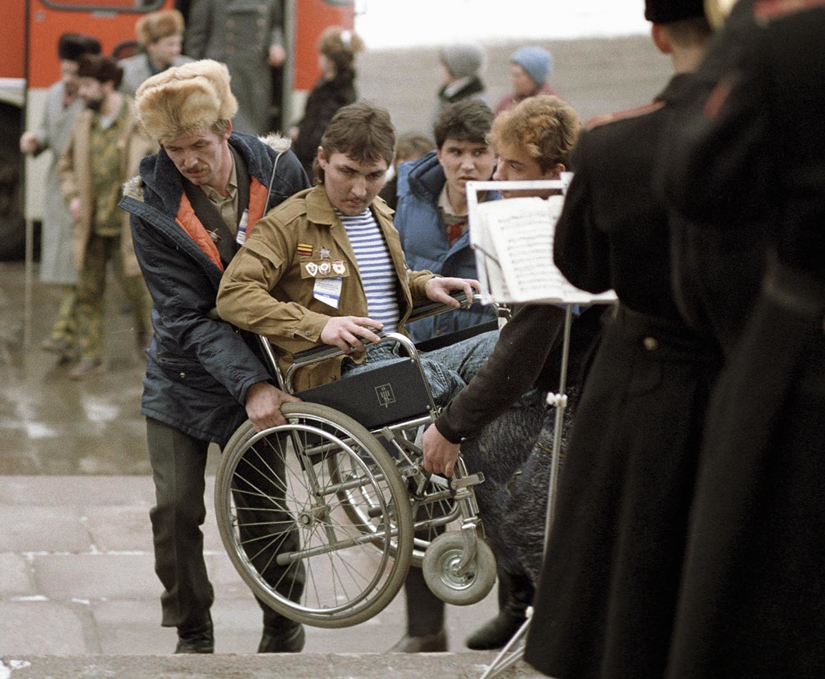 Mehrere Personen helfen einem behinderten Veteranen aus dem Afghanistan-Krieg, die Treppe in seinem Rollstuhl hinaufzukommen, 1990.
