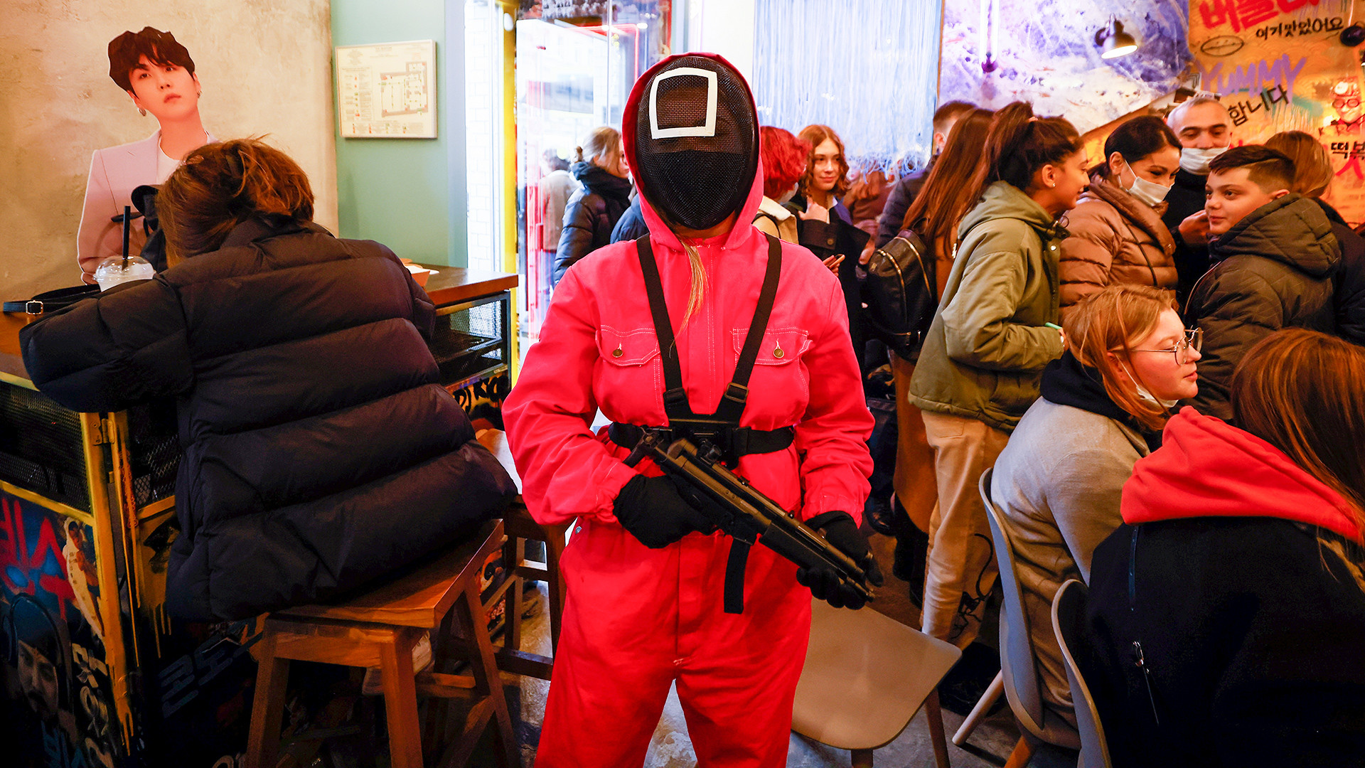 A waiter of Korean cafe Chick O'Rico in a costume of a personage from television series Squid Game aims a toy gun at a visitor in Moscow