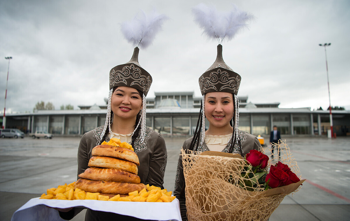 Duas jovens em trajes tradicionais aguardam com flores e comida a chegada ao aeroporto de Bichkek, no Quirguistão
