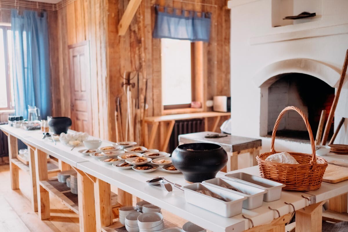 Ruska rustikalna miza s pečjo in hrano in posodo iz litega železa v leseni hiši.