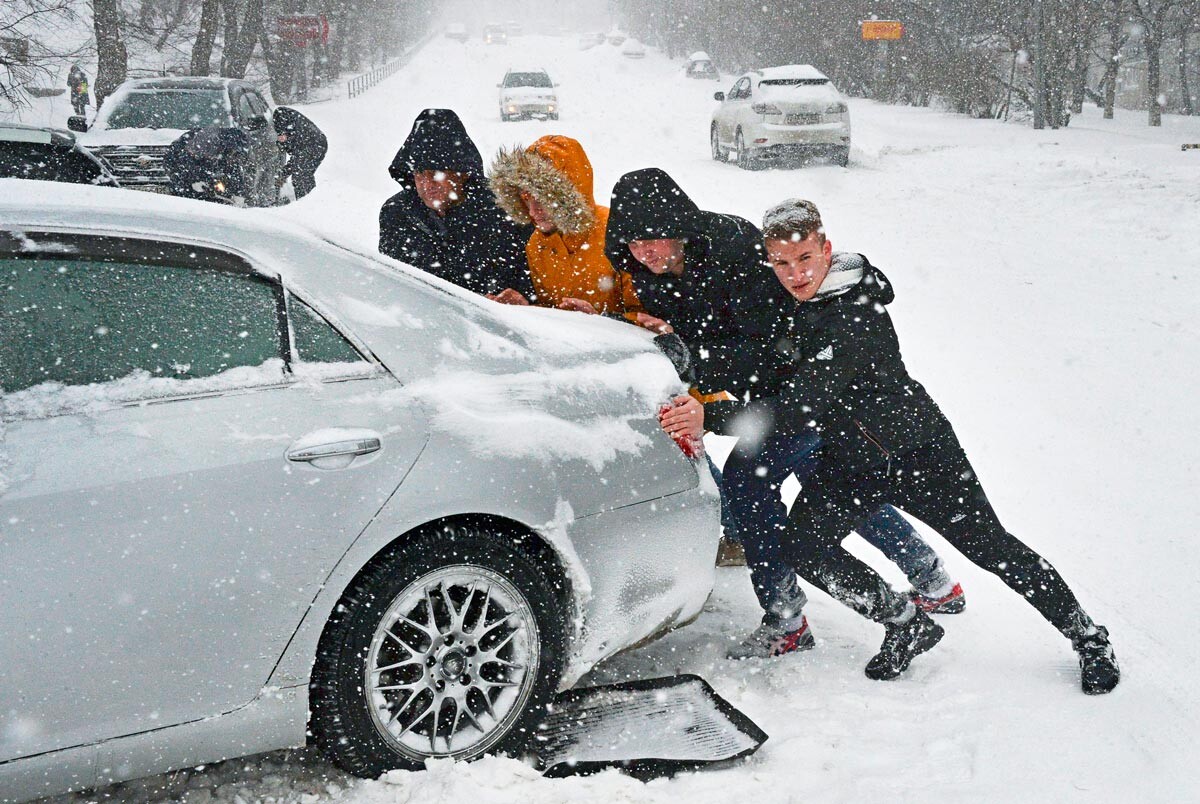 Ragazzi spingono un'auto a Valdivostok, in Russia