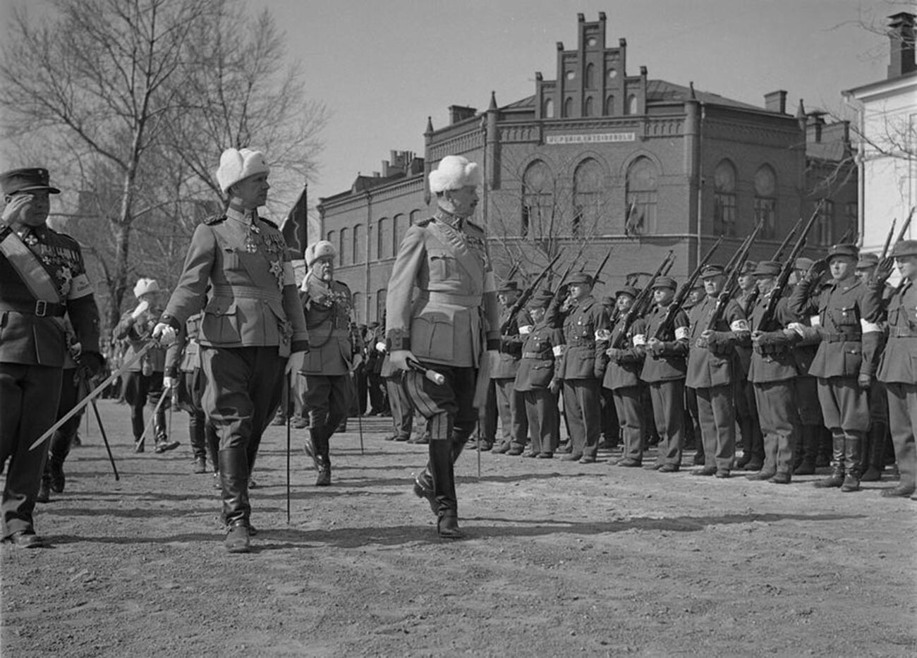 Maršal Mannerheim si ogleduje parado ob 20. obletnici osvoboditve Viborga pred  šolo v Viborgu v središču mesta. Zraven poveljuje generalpodpolkovnik Harald Öhqvist. Poleg njega je poveljnik bele garde Lauri Malmberg, zadaj med drugimi generalmajor Hannes Ignatius. 