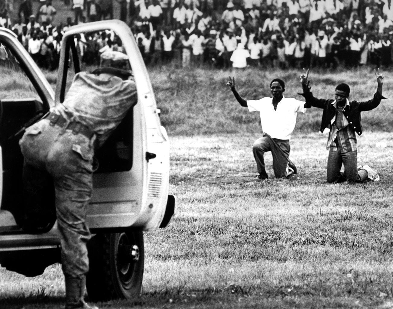 Jugendliche aus Soweto knien vor der Polizei und halten ihre Hände in die Luft, um das Friedenszeichen zu zeigen, am 16. Juni 1976 in Soweto, Südafrika.