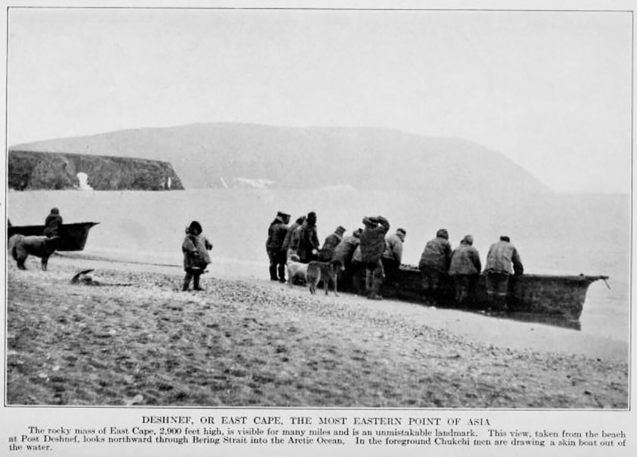 Chukchi men at Port Dezhnev bringing a umiak up on the beach; Cape Dezhnev headland in background.