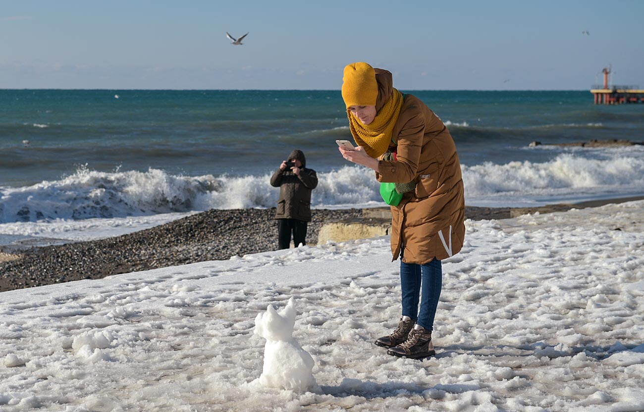 Garota fotografa uma gatinho de neve em praia no distrito de Adler, em Sochi