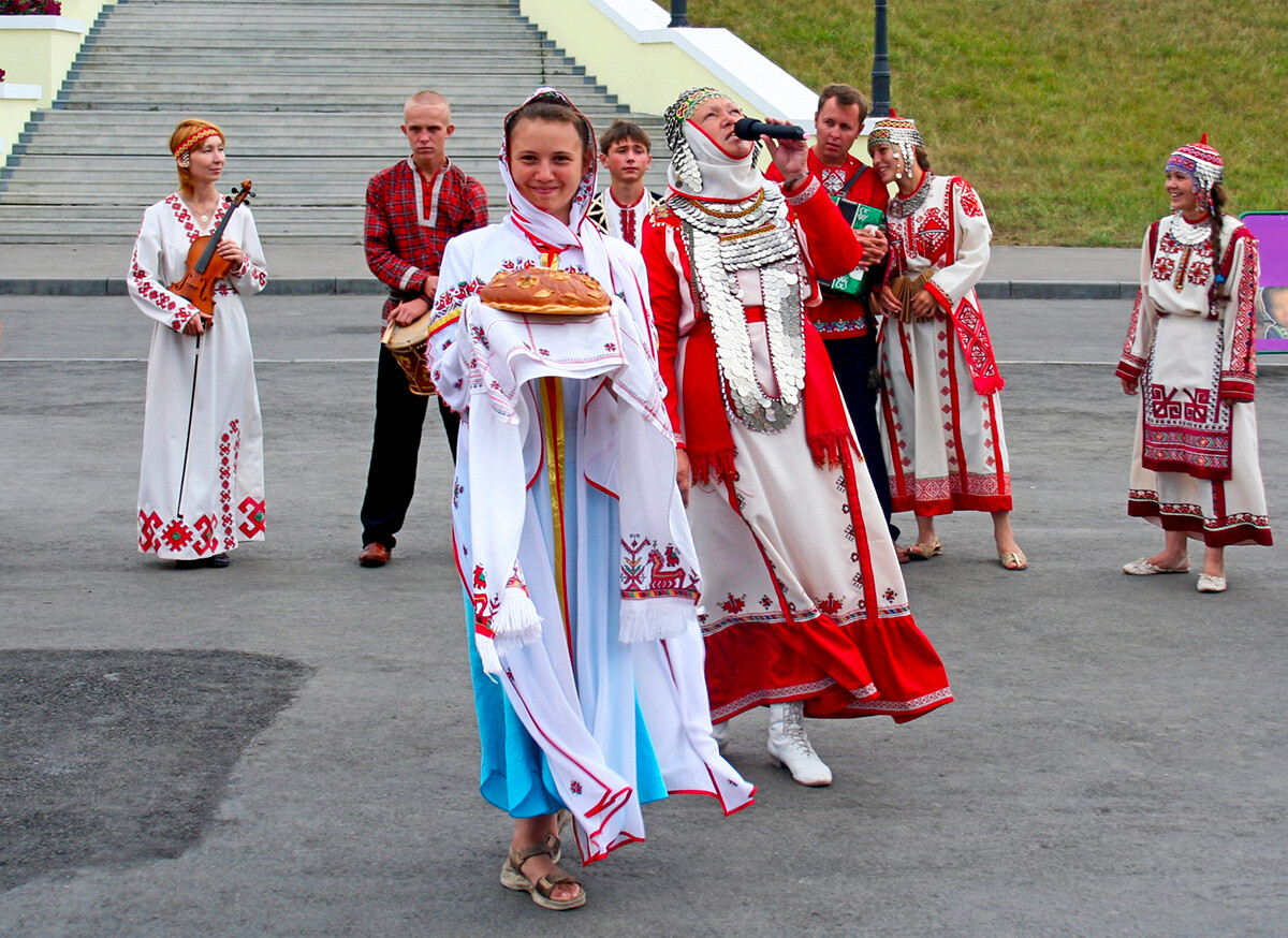 Un gruppo folkloristico della Ciuvascia accoglie un gruppo di visitatori sull'argine del fiume Volga a Cheboksarij