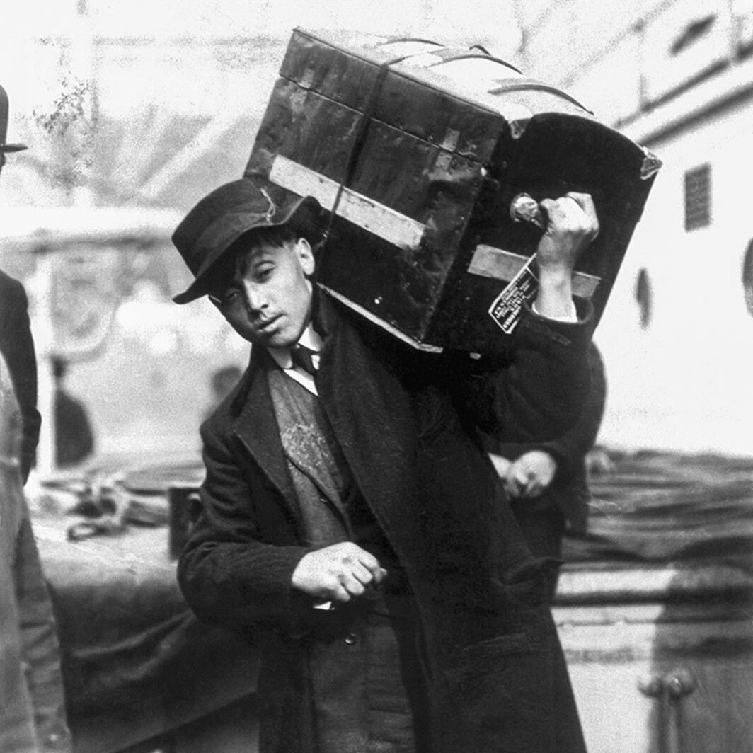 Ein junger polnischer Einwanderer trägt einen Koffer an Bord der President Grant in Ellis Island, New York, 1907. 