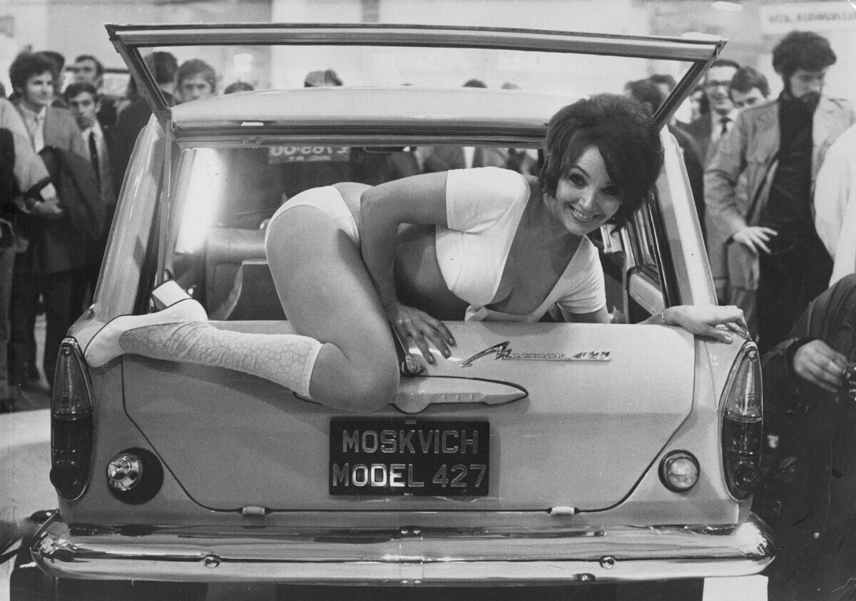 Julie Desmond, model berusia 24 tahun, naik dari belakang mobil Moskvich 427 Rusia, di pameran dagang mobil. 1971.