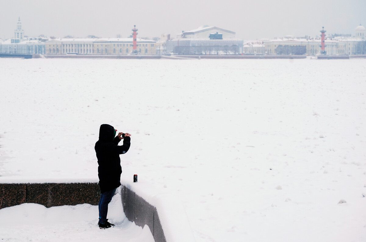 Moški na sprehodu fotografira razgled na Sankt Peterburg z nabrežja Dvorcòvaja naberežnaja po sneženju