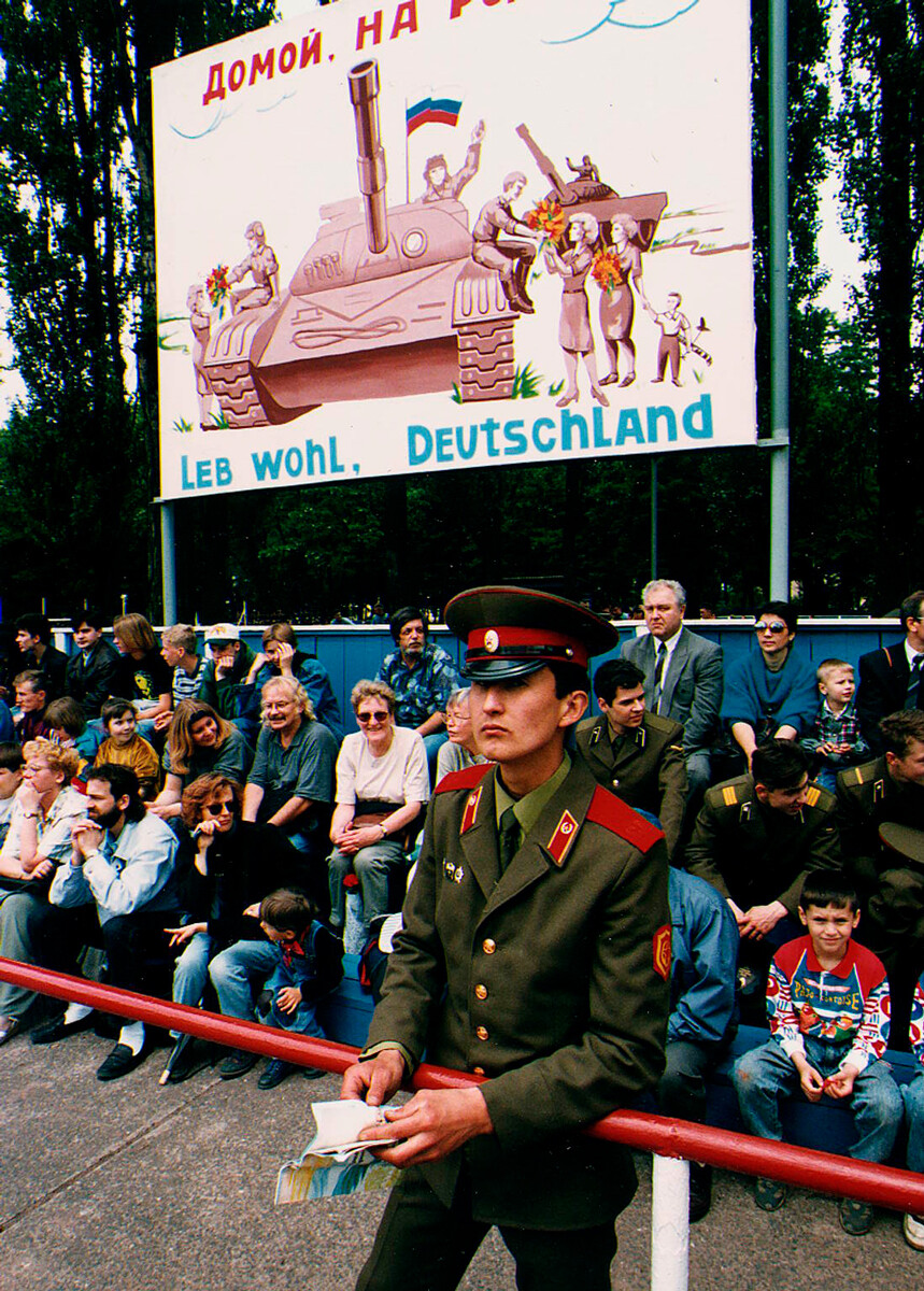 Ein Soldat und Teilnehmer des Abschiedsfestes unter einem Plakat „Leb wohl, Deutschland“ 1994 