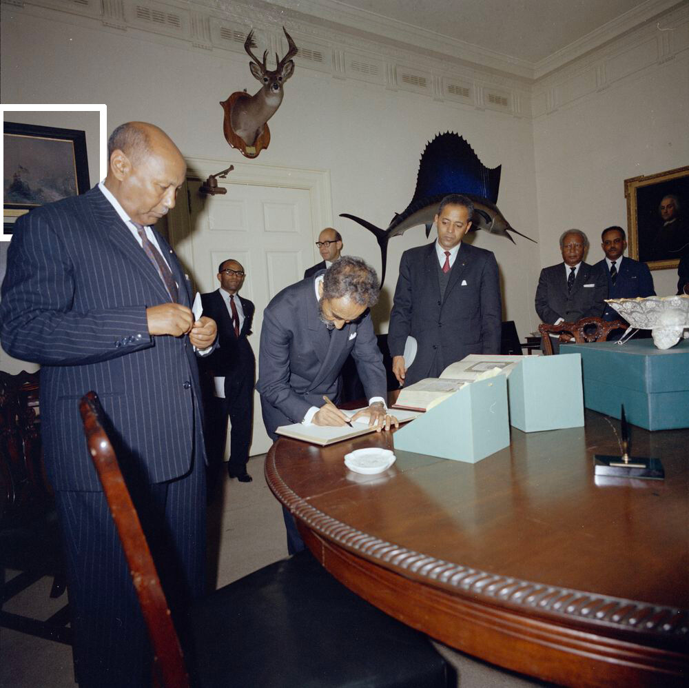 Kaisar Etiopia, Haile Selassie I, menulis dalam sebuah buku saat pertukaran hadiah dengan Presiden John F. Kennedy di Fish Room Gedung Putih.