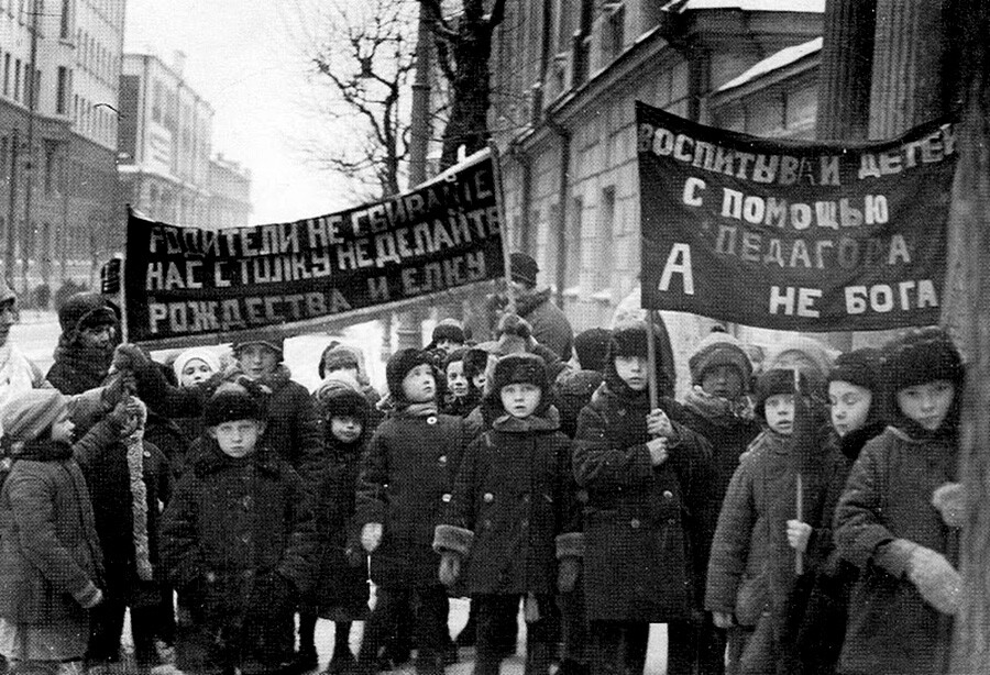 Demonstrasi anak-anak anti-Natal, 1929. Spanduk di sebelah kiri bertuliskan “Orang tua, jangan buat kami bingung — jangan buat perayaan Natal”; di sebelah kanan: “Besarkan anak-anak Anda dengan bantuan guru, bukan Tuhan”.