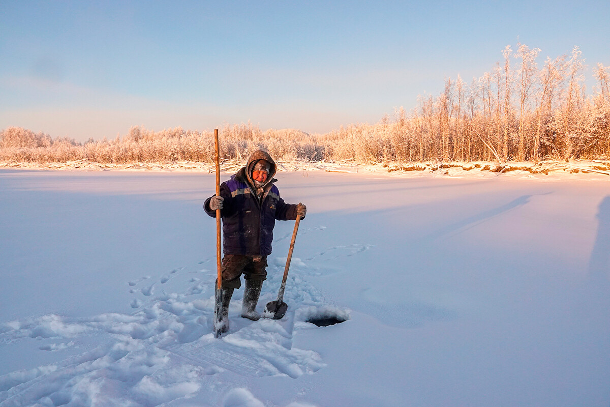 Un abitante della Jacuzia, pesantemente vestito per affrontare la temperatura di -60 ºC, si appresta a pescare nel buco nel ghiaccio appena aperto