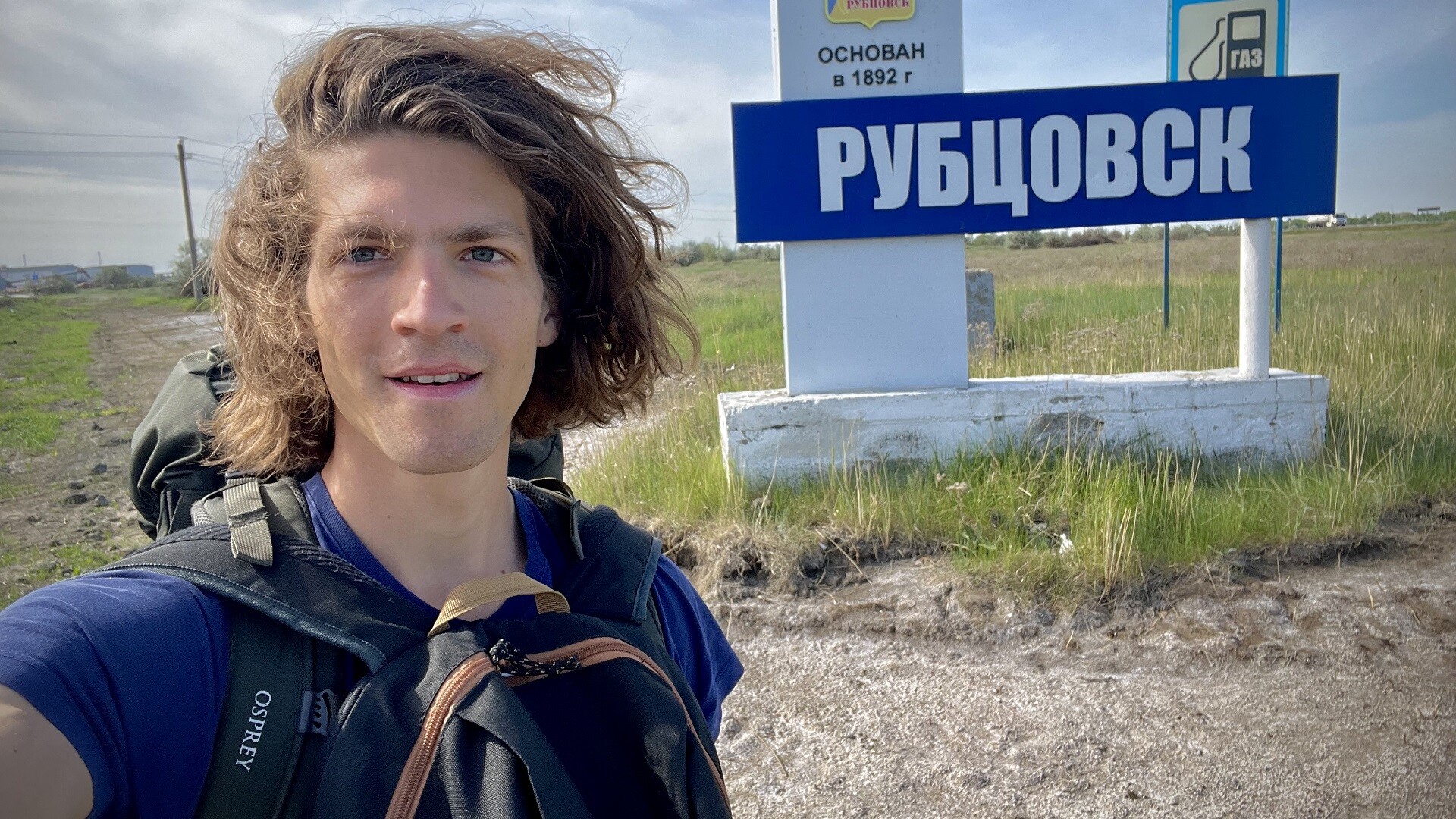 Lo studente svizzero Etienne Steinemann davanti al cartello della città di Rubtsovsk, nel Territorio dell’Altaj, da dove ha iniziato il suo lungo autostop che lo ha portato fino a Vladivostok