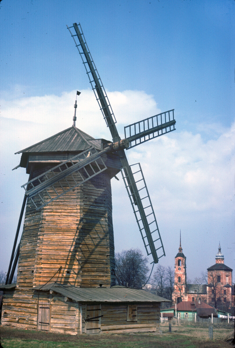 Log windmill with rotating top. Originally built in 19th century at Moshok village, Sudogodsky Region. Background: brick Church of Sts. Boris & Gleb (1749). April 27, 1980