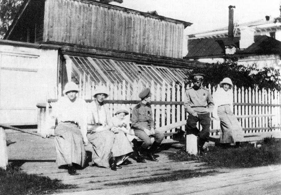 El zar Nicolás II y sus hijos sentados frente a una valla y un invernadero durante su cautiverio en Tobolsk. (de izquierda a derecha): Tatiana, Olga, un pequeño criado, Alexéi, Nicolás II y Anastasíya.