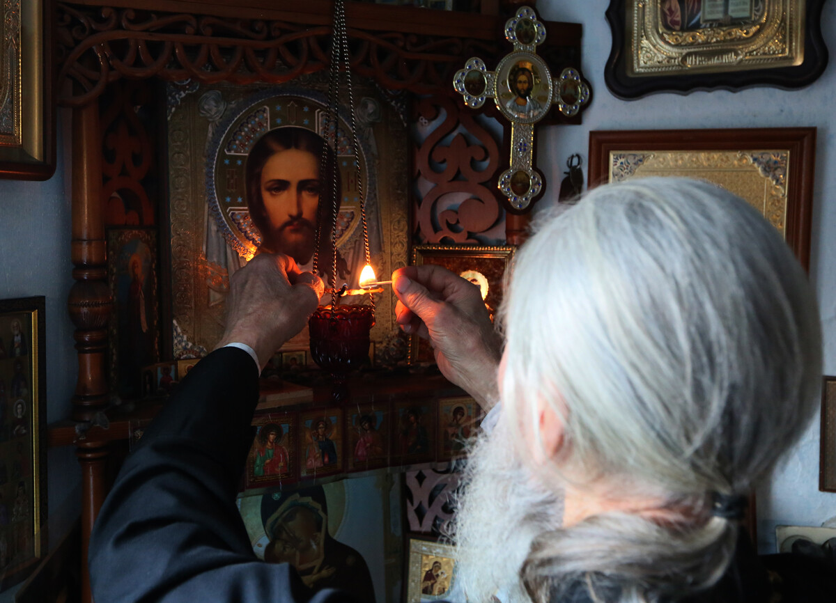 Un sacerdote ortodosso accende la lampada votiva dell’iconostasi in una chiesa di campagna del Territorio di Krasnojarsk, in Siberia