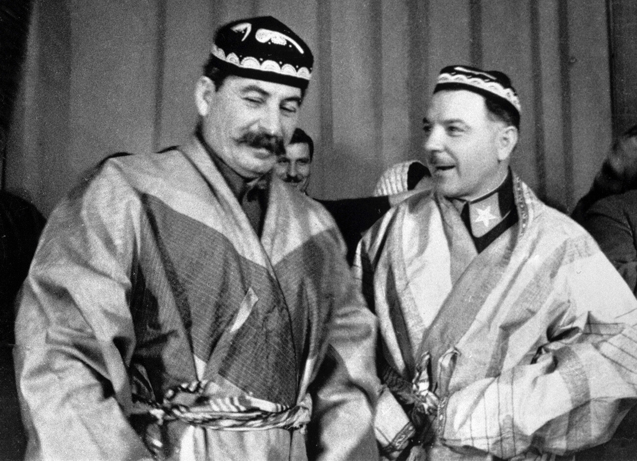 Stalin and Voroshilov wearing ethnic costumes presented to them by delegates from a conference of advanced collective farmers of Turkmenistan and Tajikistan.