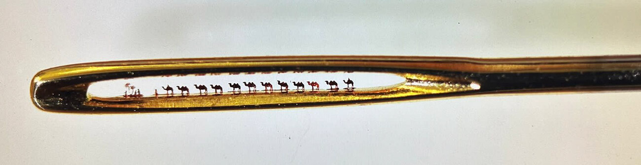 Camel caravan in the eye of a needle. Figurines of camels and herders are made of gold. Height 0.25 mm