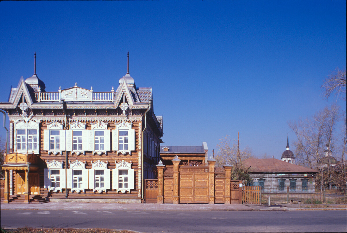 Maison Chastine, 21, rue Engels. L’un des meilleurs exemples de l’architecture décorative sibérienne en bois. Le cœur de la maison a été construit vers 1840 et agrandi par la suite. En 1907, elle a été achetée par Apolos Chastine qui a ajouté un étage. En arrière-plan: église de la Transfiguration