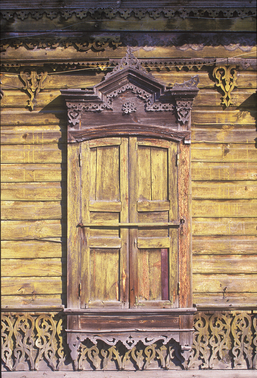 Maison en bois située au 50 de la rue Tara. Fenêtre fermée par des volets et décoration chantournée. Photographie prise par William Brumfield le 15 septembre 1999