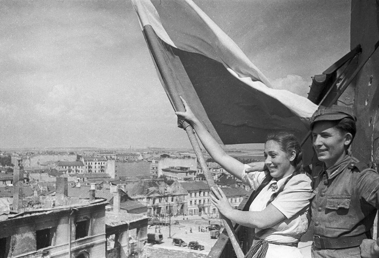 Soldado do Exército polonês e uma moradora de Lublin erguem uma bandeira sobre a cidade libertada, agosto de 1944.