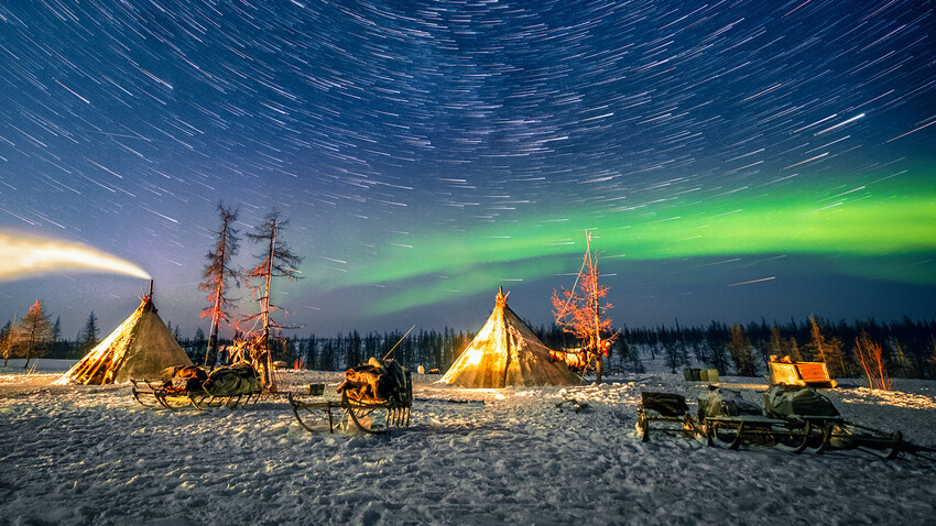 Acampamento de povos nômades nenets com tenda tradicional (chamada tchum) e trenós na planície coberta de neve, na península de Iamal.