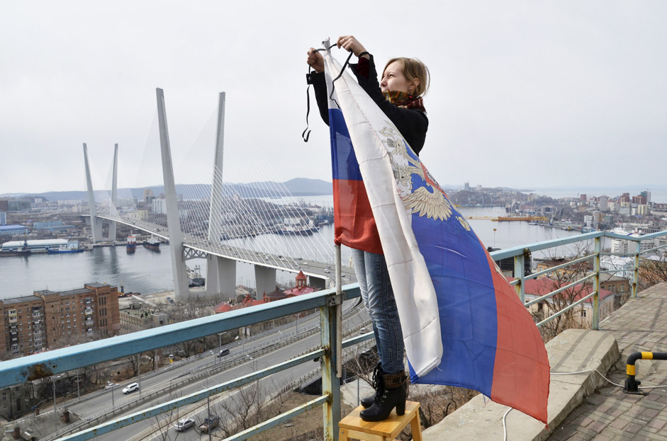 A woman attaches a black ribbon for those killed in the sinking of Dalniy Vostok, to a Russian national flag in Vladivostok April 7, 2015. A Russian trawler Dalniy Vostok sank in the Sea of Okhotsk off Russia's far eastern Kamchatka peninsula on April 2, 2015, killing at least 56 of the 132 crew, the emergencies ministry said on April 2. 