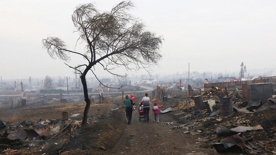 Family members walk away while passing the debris of destroyed buildings in the settlement of Shyra, damaged by recent wildfires, in Khakassia region, April 13, 2015. More than 20 villages and towns have been damaged by the fires that have been burning for several days in dry and windy weather.