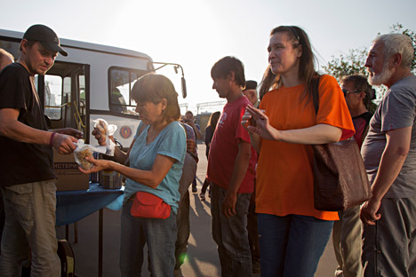 A crowd of homeless people gradually gathers outside the fence waiting for their dinner.