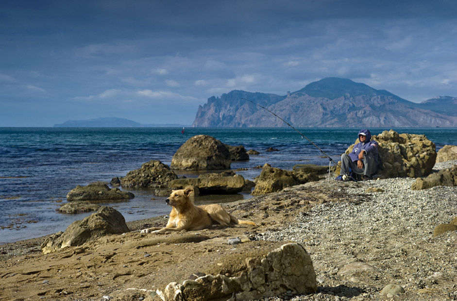 Рибар и неговото куче на брега в населеното място Орджоникидзе в Крим.