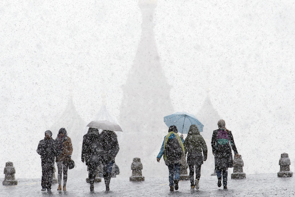 Луѓе шетаат по Црвениот плоштад на првиот снег од кој во позадината одвај се гледа храмот на Василиј Блажени во Москва.