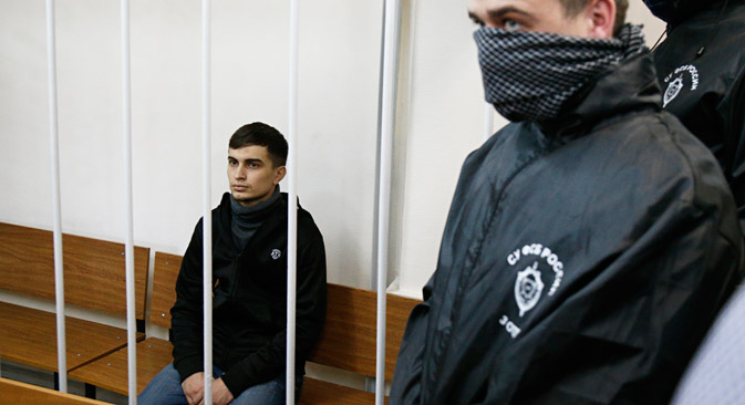 Aslan Baisultanov, a man suspected of plotting a terrorist attack in Moscow, sits in a defendants' cage as two intelligence officials with their faces covered, stand in a court room in Moscow, Oct. 13, 2015. Source: AP