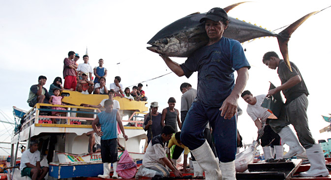 Fishermen and their families watch as a worker carries a yellow fin tuna off a fishing boat at fish at a port in General Santos City, Mindanao, southern Philippines January 10, 2008. The Philippines is one of the biggest tuna producing countries in the world and most of its exports are through General Santos, a port city on the archipelago's southern tip.