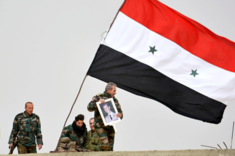 A fighter loyal to Syria's president Bashar Al-Assad holds his picture as fellow fighters rest by a Syrian national flag after gaining control of the area in Deir al-Adas, a town south of Damascus, Daraa countryside February 10, 2015. 
