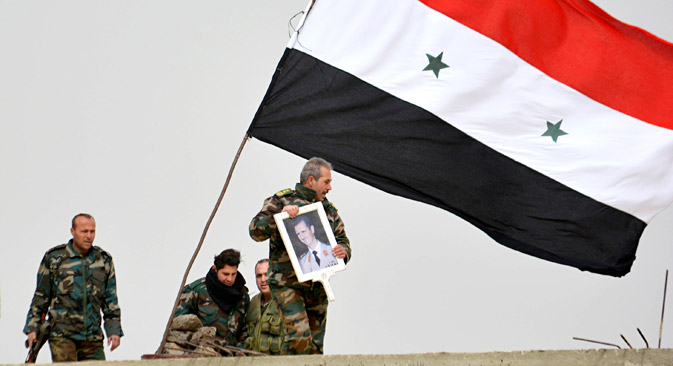 A fighter loyal to Syria's president Bashar Al-Assad holds his picture as fellow fighters rest by a Syrian national flag after gaining control of the area in Deir al-Adas, a town south of Damascus, Daraa countryside February 10, 2015. Syrian government troops and their allies in the Lebanese group Hezbollah pressed a major offensive in southern Syria on Wednesday, taking new ground in a campaign against insurgents who pose one of the biggest remaining threats to Damascus. Syrian state TV broadcast live from Deir al-Adas, a town some 30 km (19 miles) south of Damascus that it said had been captured. The sound of artillery being fired could be heard. The nearby town of Deir Maker was also captured, state TV said. Picture taken February 10, 2015.