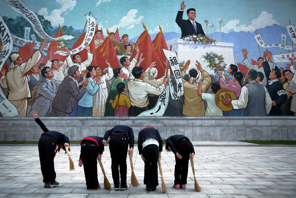School girls bow before a mural of Kim Il Sung in North Korea.