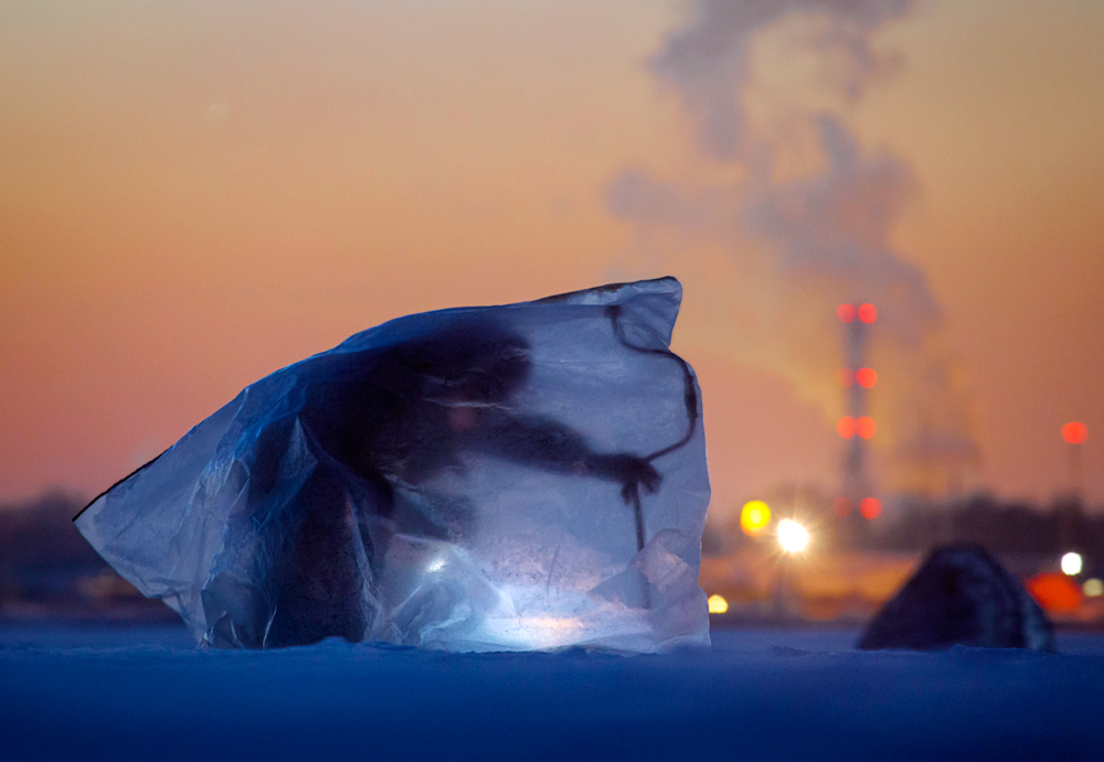 A man covered with plastic bag for protection from the wind and cold, fishes through an ice hole in the Finnish Gulf west of St.Petersburg, Russia