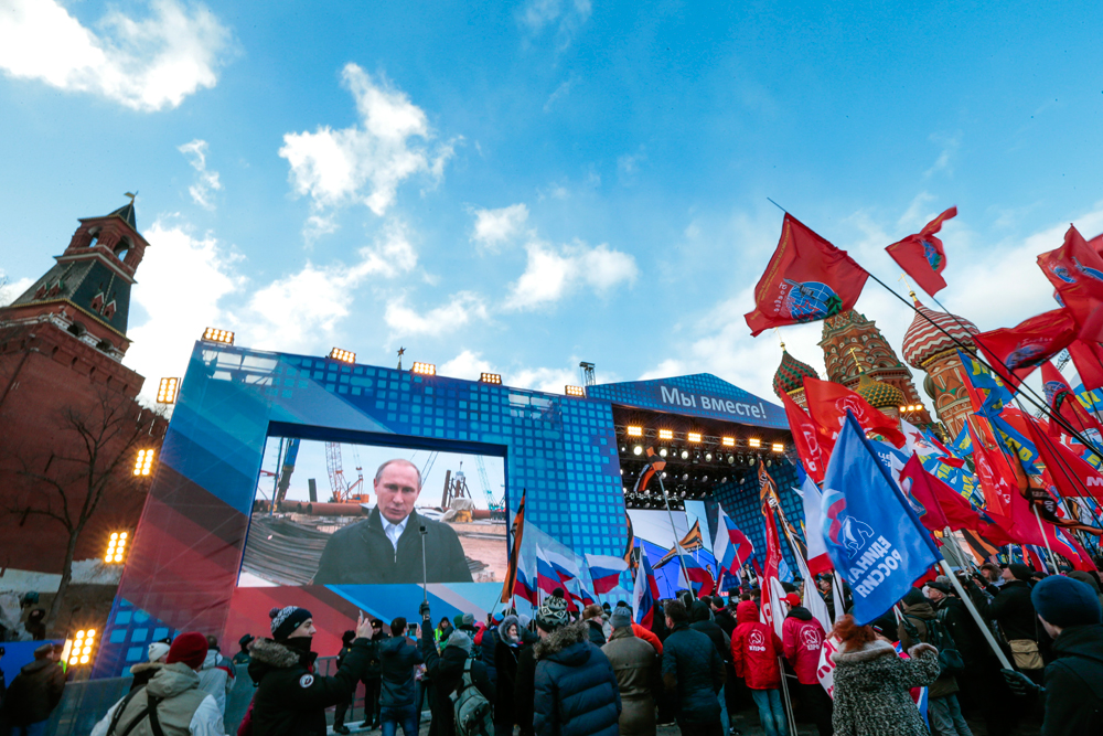 Orang-orang mendengarkan Presiden Rusia Vladimir Putin berpidato dari lokasi pembangunan jembatan Selat Kerch di Pulau Tuzla, selama perayaan dua tahun bergabungnya Krima ke Rusia di Lapangan Merah, Moskow, Rusia 18 Maret 2016.