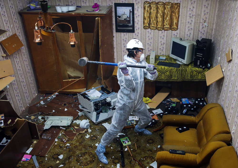 A man in a hard hat smashes household objects in a rage room. The Debauch stress relief service gives its customers an opportunity to smash the rage room up with sledgehammers and bats to relieve stress and tension.
